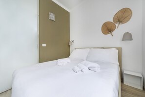 A neatly made bed with white linens and towels, a wooden headboard, and two wall-mounted lamps.