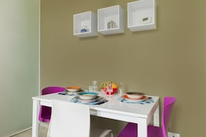 A dining area with a white table set for two, surrounded by purple chairs. There are three white wall-mounted shelves above the table. - UR-NEST Mitelli, a bedroom (Bologna)