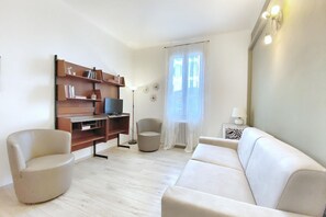 Ein Wohnzimmer mit einer Couch, einem Sessel, einer TV-Konsole und einem Bücherregal.