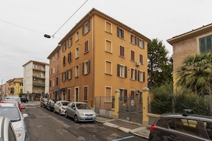 A multi-story residential building with a yellow facade, parked cars along the street, and a visible parking sign.