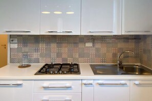 Eine moderne Küche mit weißen Schränken, einer gemusterten Spritzschutzwand, einem Gasherd und einer Spüle aus Edelstahl.