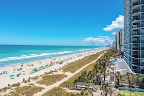 A beach view with a hotel building, beach umbrellas, and a clear sky.