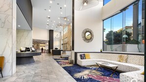A modern lobby with a reception desk, seating area, and large windows offering a view of the outside. - Ruby Apartments - Q Stay (Surfers Paradise)