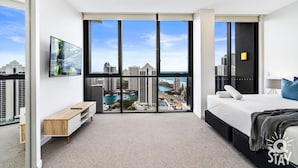 A modern hotel room with a large sliding glass door leading to a balcony with a city view. - Ruby Apartments - Q Stay (Surfers Paradise)