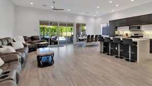 A spacious living area with a sofa set, a coffee table, and a dining area with chairs and a table. There is a kitchen with a microwave and a bar area with stools. - Multi month discount,luxury,entertaining +relaxing (Cathedral City)