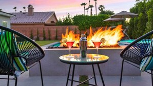 An outdoor patio with a fire feature, two chairs, and a table with a cocktail and a bottle. - Multi month discount,luxury,entertaining +relaxing (Cathedral City)