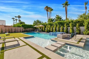 A swimming pool with a hot tub, lounge chairs, and palm trees.