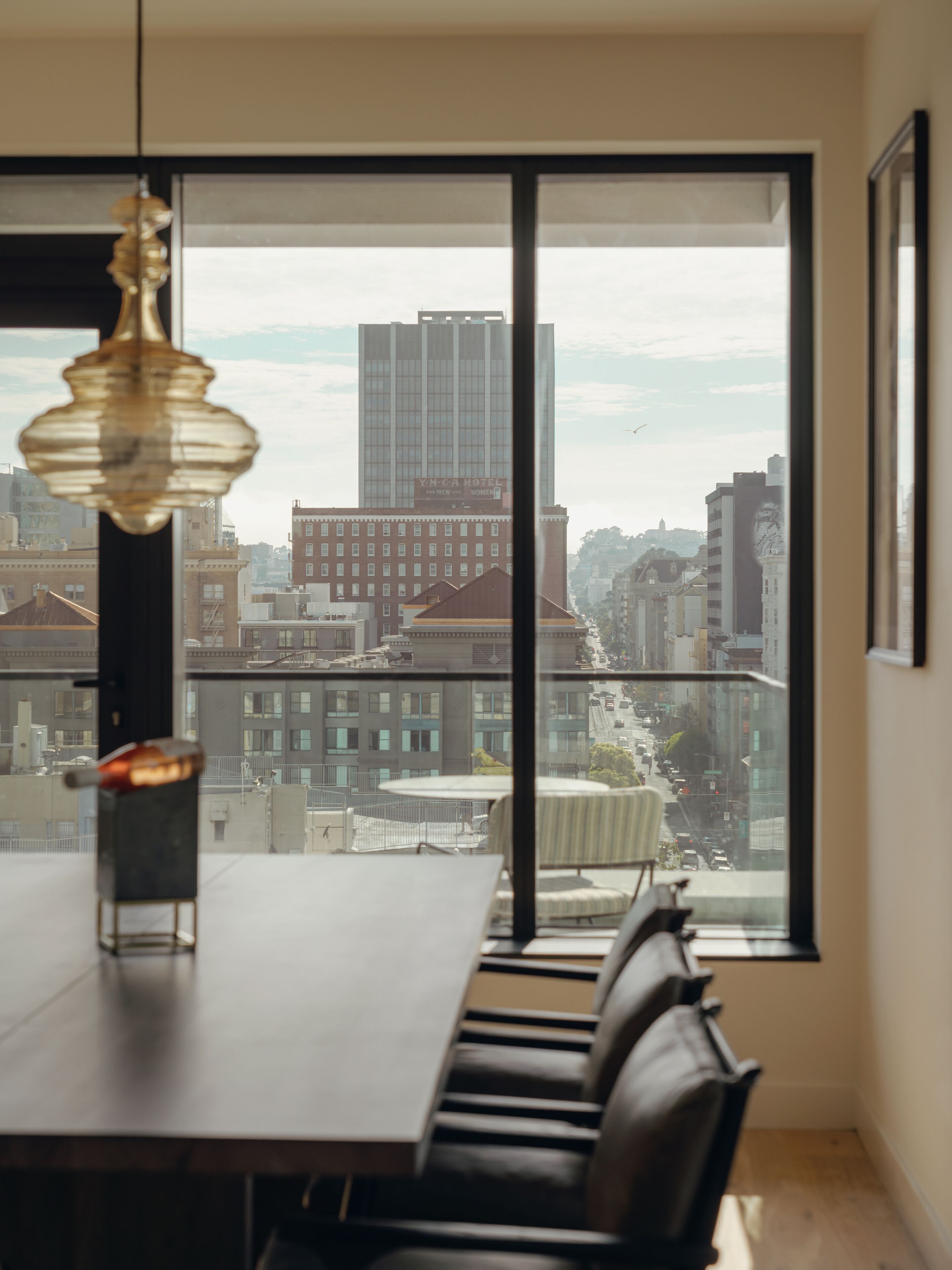 A modern dining area with a large window, a table, chairs, and a hanging light fixture.