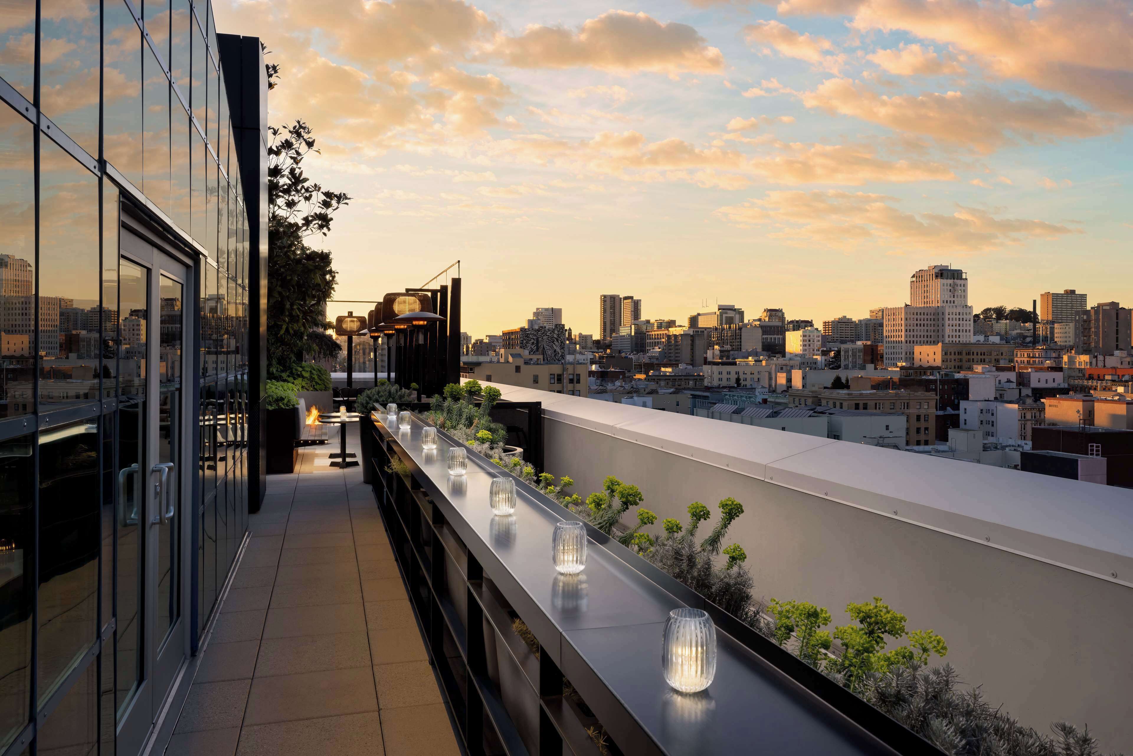 Terraza en la azotea con vista al horizonte urbano, barandillas de vidrio e iluminación exterior.