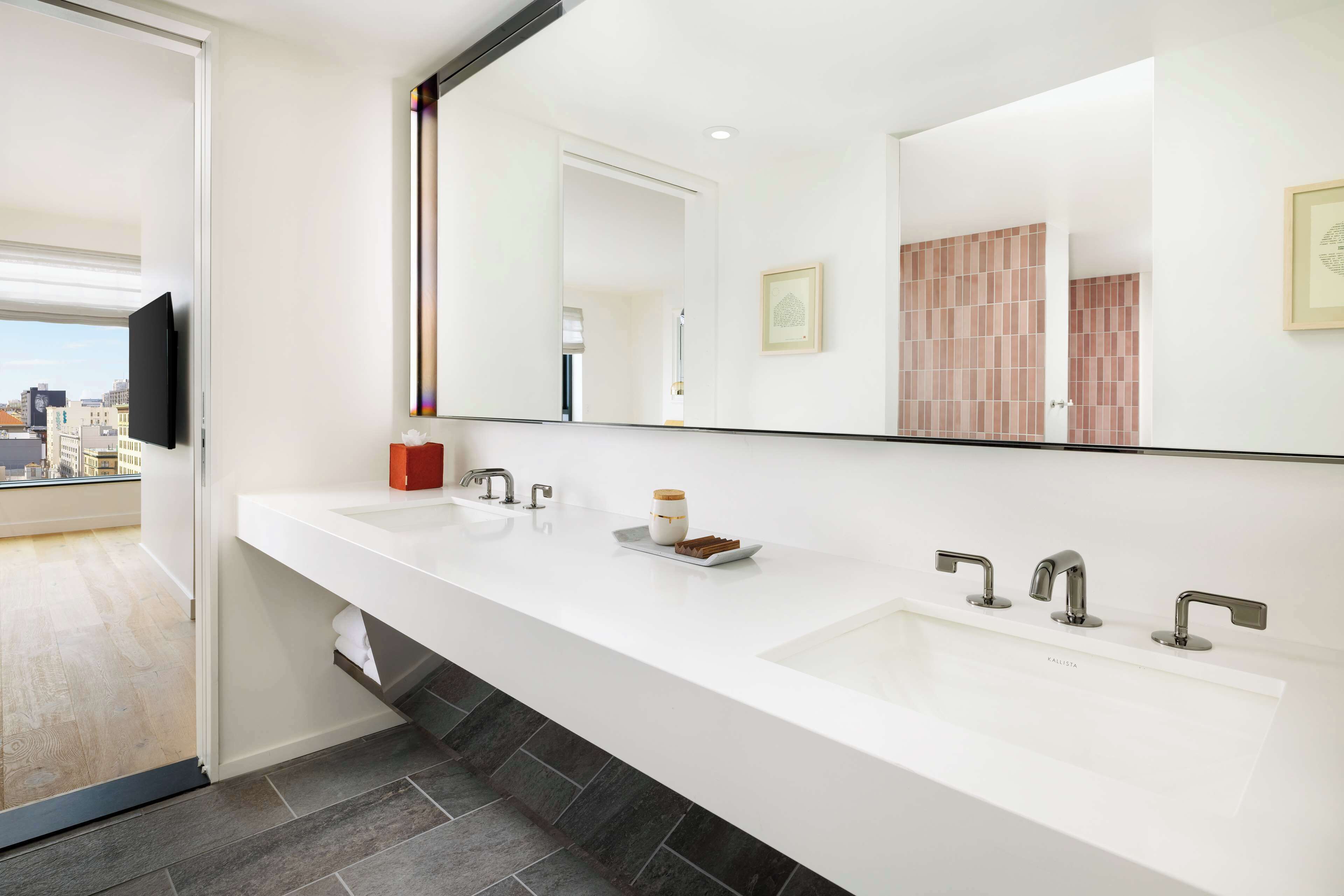 A modern bathroom with a large mirror, two sinks, and a window overlooking a cityscape.