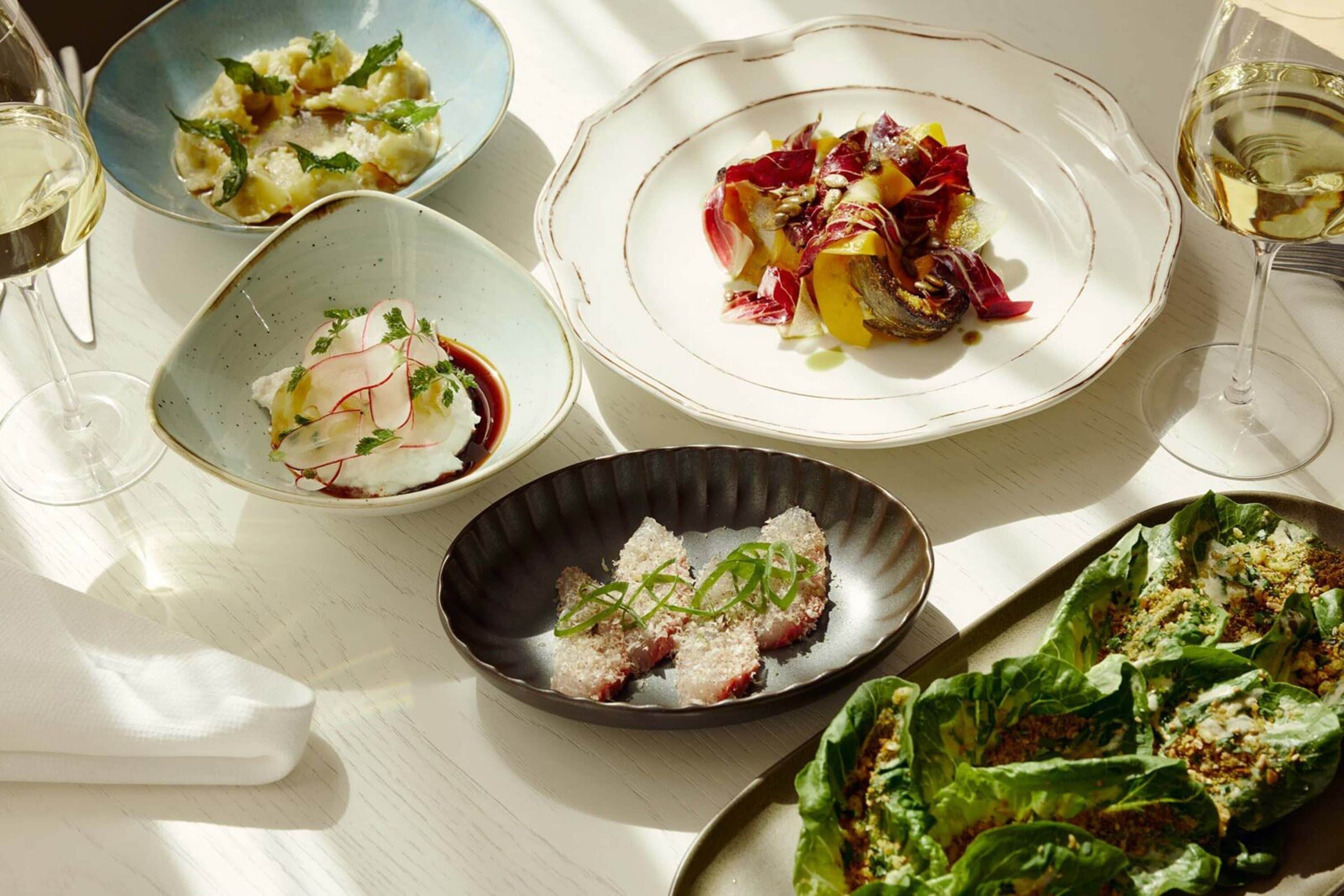A table with various dishes and glasses of white wine.