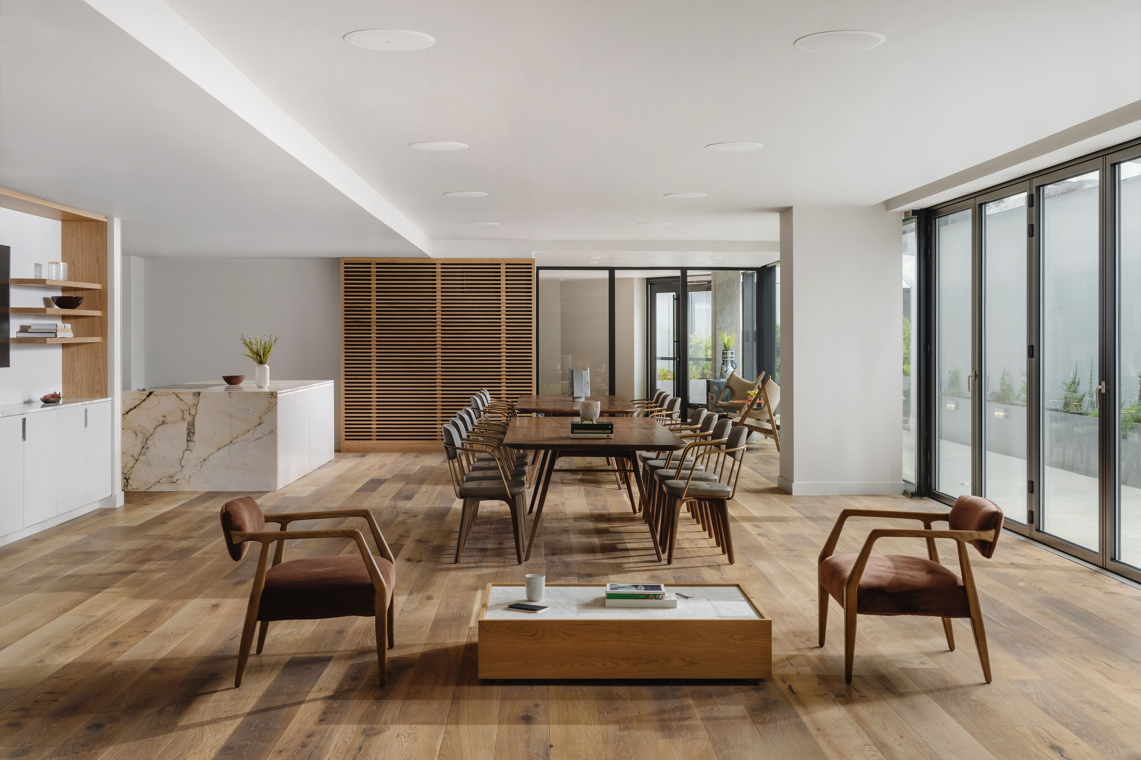 A modern dining area with a wooden table and chairs, a marble countertop, and large windows offering a view.