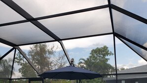 A covered outdoor swimming pool area with two lounge chairs and a blue umbrella. - Free Heated Saltwater Pool, Kayaks, Bikes, Tennis Rackets and Fishing Poles! (North Port)