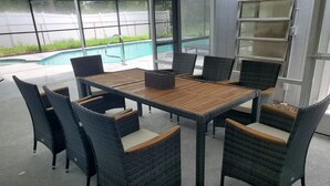 An outdoor patio with a pool, surrounded by wicker furniture and a glass door. - Free Heated Saltwater Pool, Kayaks, Bikes, Tennis Rackets and Fishing Poles! (North Port)