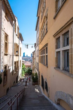 A narrow street flanked by historic buildings with a clear view of a modern city skyline in the distance.