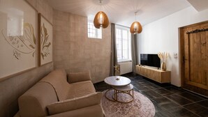 Ein Wohnzimmer mit einer Couch, einem runden Couchtisch, einem Fernseher auf einem Holzboden und einem großen Fenster mit Vorhängen.