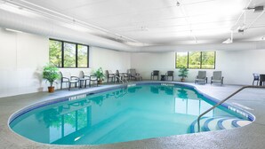 Une piscine intérieure à l’eau d’un bleu cristallin, entourée de chaises longues et de plantes en pot.