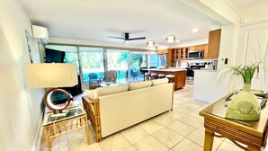 A living room with a sofa, a dining table, and a kitchen in the background. - Tropical Oasis By The Sea (Lahaina)