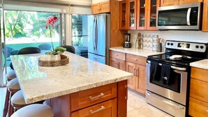 A modern kitchen with wooden cabinets, stainless steel appliances, a marble countertop, and pendant lighting. - Tropical Oasis By The Sea (Lahaina)