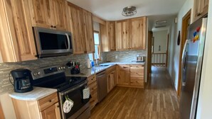 A kitchen with wooden cabinets, a stainless steel refrigerator, a microwave, and a stove. - 2 Bedroom Coach House, Green Lake, WI (Green Lake)