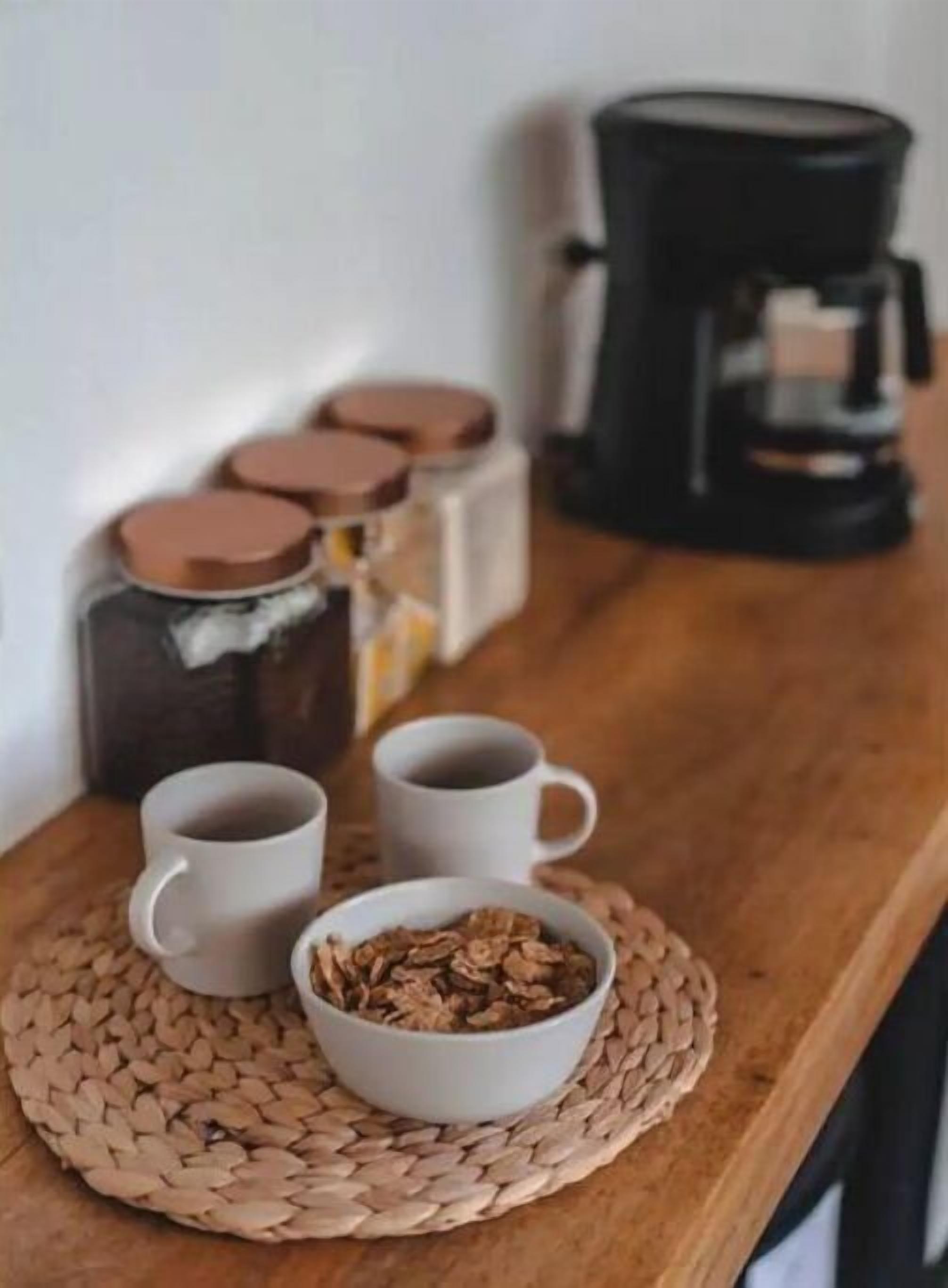 A kitchen counter with a coffee maker, two white cups, and a bowl of cereal.