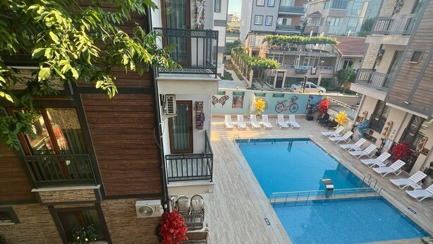Area piscina sul tetto con sedie a sdraio e tavoli, circondata da edifici.