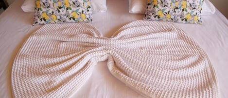 A bed with a large, textured white blanket and two pillows with a lemon and floral pattern.