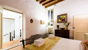 Una camera da letto con un letto, un termosifone, una finestra, un soffitto in legno e una porta.
