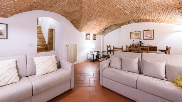 Un soggiorno con due divani, soffitto in mattoni, pareti bianche e una scala che conduce a un piano superiore.