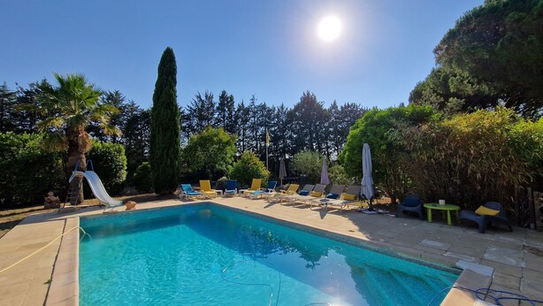 Ein Swimmingpool mit Liegestühlen und Sonnenschirmen, umgeben von Bäumen und blauem Himmel.