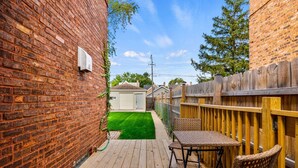 A wooden deck with a brick wall, a small lawn, and a wooden fence. - Enjoy Chicago/suburbs 2BR townhouse fully equipped (Chicago)