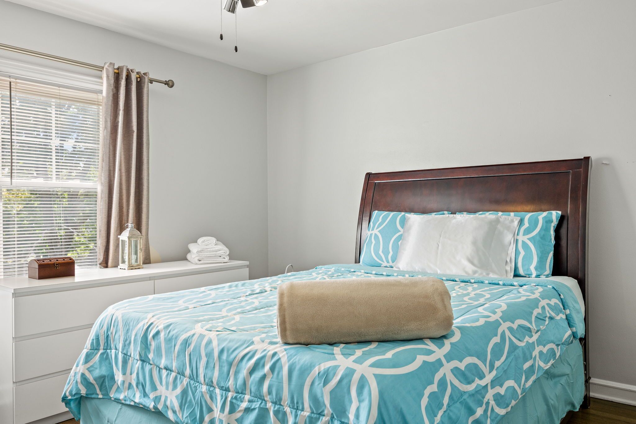 Un dormitorio con cama, mesita de noche, ventana con cortinas y vistas al exterior.