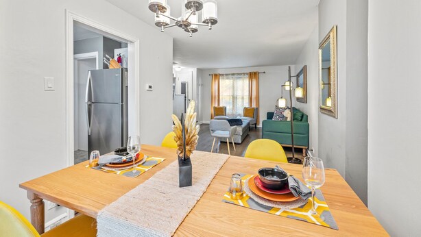 A modern dining area with a wooden table set for two, a chandelier, and a view into the living room. - Enjoy Chicago/suburbs 2BR townhouse fully equipped (Chicago)