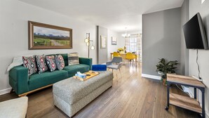 A modern living room with a green sofa, a patterned ottoman, and a dining area with yellow chairs. - Enjoy Chicago/suburbs 2BR townhouse fully equipped (Chicago)