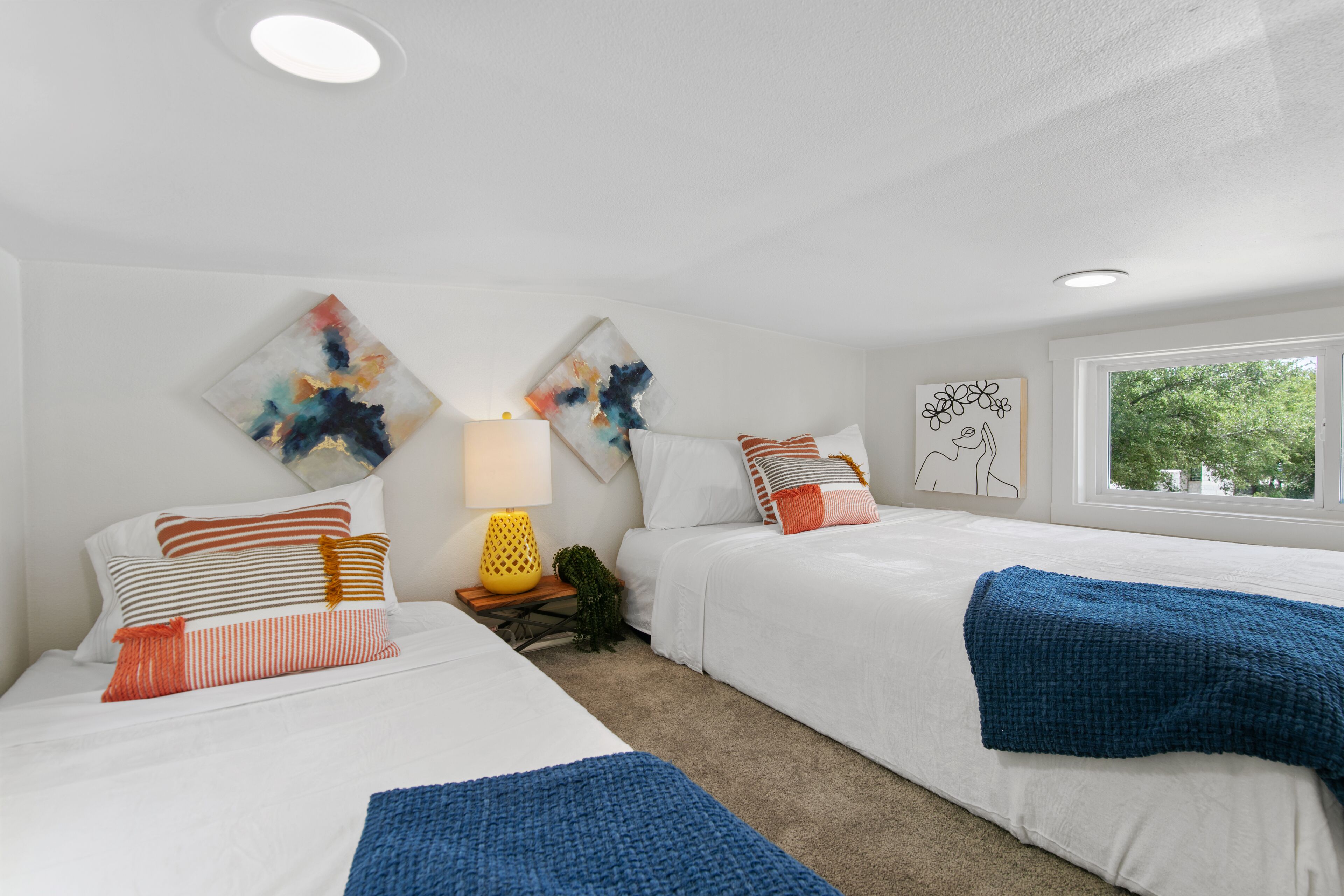 Une chambre d’hôtel moderne avec deux lits, une fenêtre donnant sur un beau paysage et des œuvres d’art abstrait accrochées aux murs.