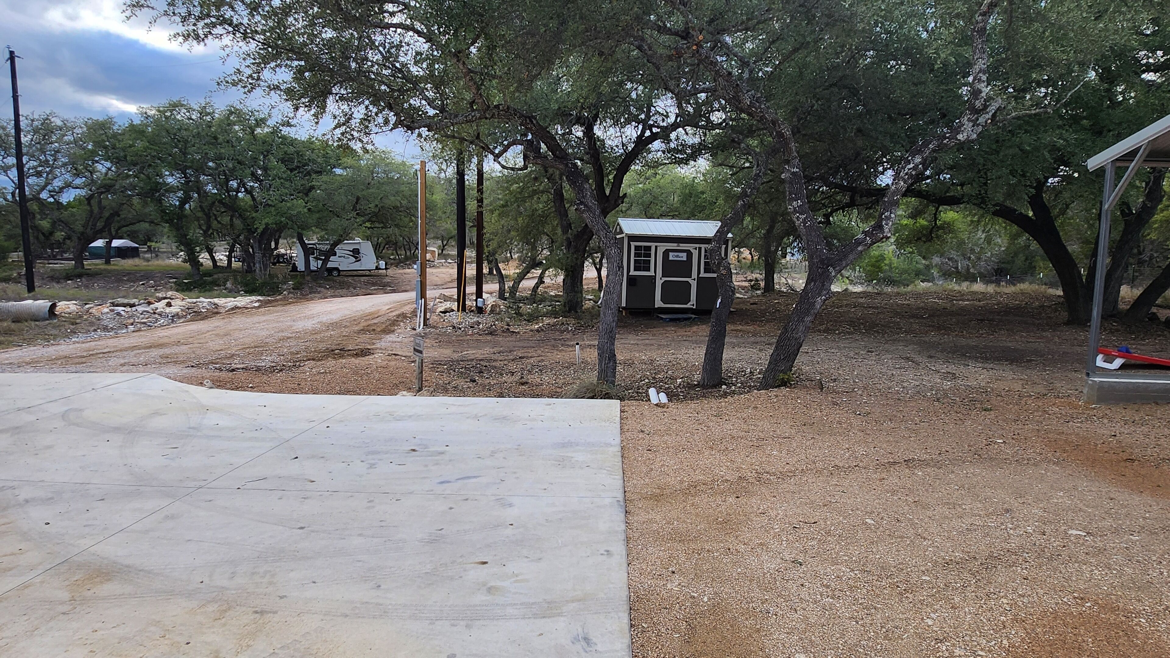 Un pequeño edificio de oficinas con techo metálico, rodeado de árboles y un camino de tierra.