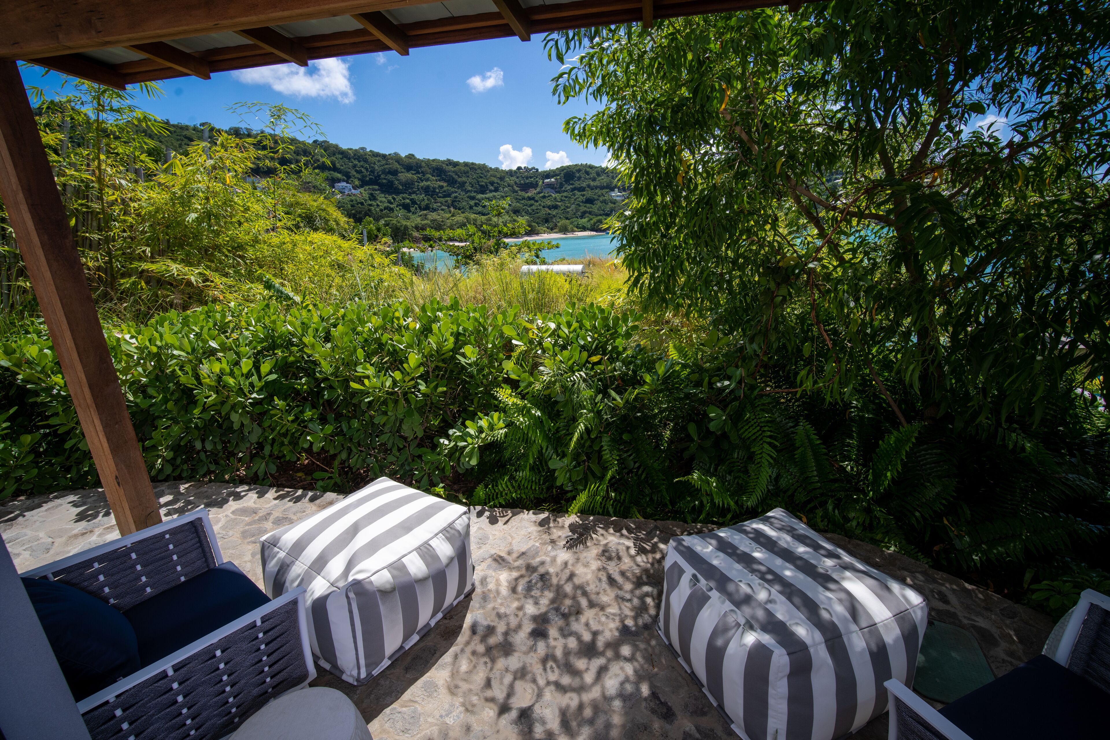 A covered outdoor seating area with striped cushions, overlooking a lush landscape and a body of water.