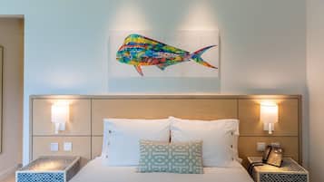 A hotel room with a bed, two bedside tables, a wall-mounted lamp, and a colorful fish artwork above the bed.