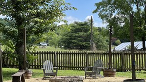 An outdoor seating area with Adirondack chairs and a fire pit, surrounded by a wooden fence and trees. - Conveniently Located Private Guesthouse in Wears Valley - No Cleaning Fees! (Sevierville)