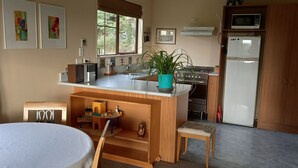 Une cuisine compacte avec un îlot central en bois, un évier, une cuisinière et un réfrigérateur. Une fenêtre laisse entrer la lumière naturelle et offre une vue sur la verdure environnante.