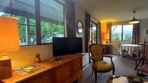 Un salon équipé d’un téléviseur, de meubles en bois, d’un coin repas et de grandes fenêtres.
