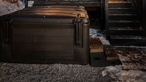 En træhytte med en overdækket veranda, et spabad og en trappe til indgangen.