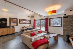 Ein modernes Wohnzimmer mit einer Couch, einem Couchtisch und einem Essbereich mit Blick auf eine verschneite Landschaft.