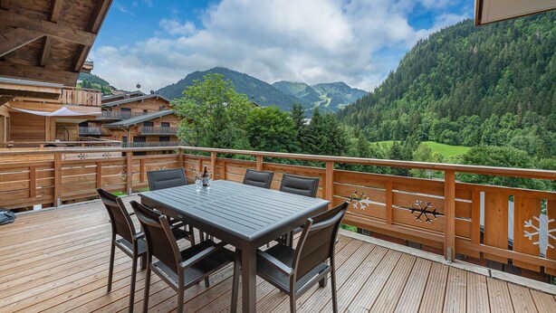 Een houten terras met een tafel en stoelen, met uitzicht op een bergachtig landschap.