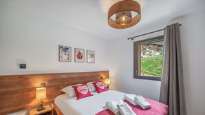 Een hotelkamer met een houten hoofdbord, een bed met witte en rode beddengoed, een rode plaid en een raam met uitzicht op een gebouw en groen.