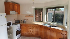 A kitchen with wooden cabinets, a stove, a microwave, and a window with a view of a brick house. - City Edge Lower Plenty (Lower Plenty)