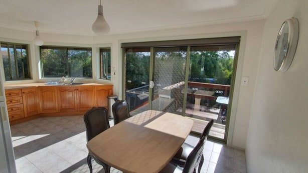 A kitchen with wooden cabinets, a dining table, and chairs. There is a large sliding glass door leading to an outdoor area with a table and chairs. - City Edge Lower Plenty (Lower Plenty)