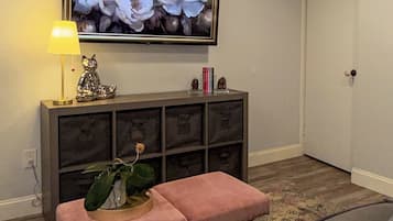 A living room with a television mounted on the wall, a bench, a lamp, and a bookshelf.