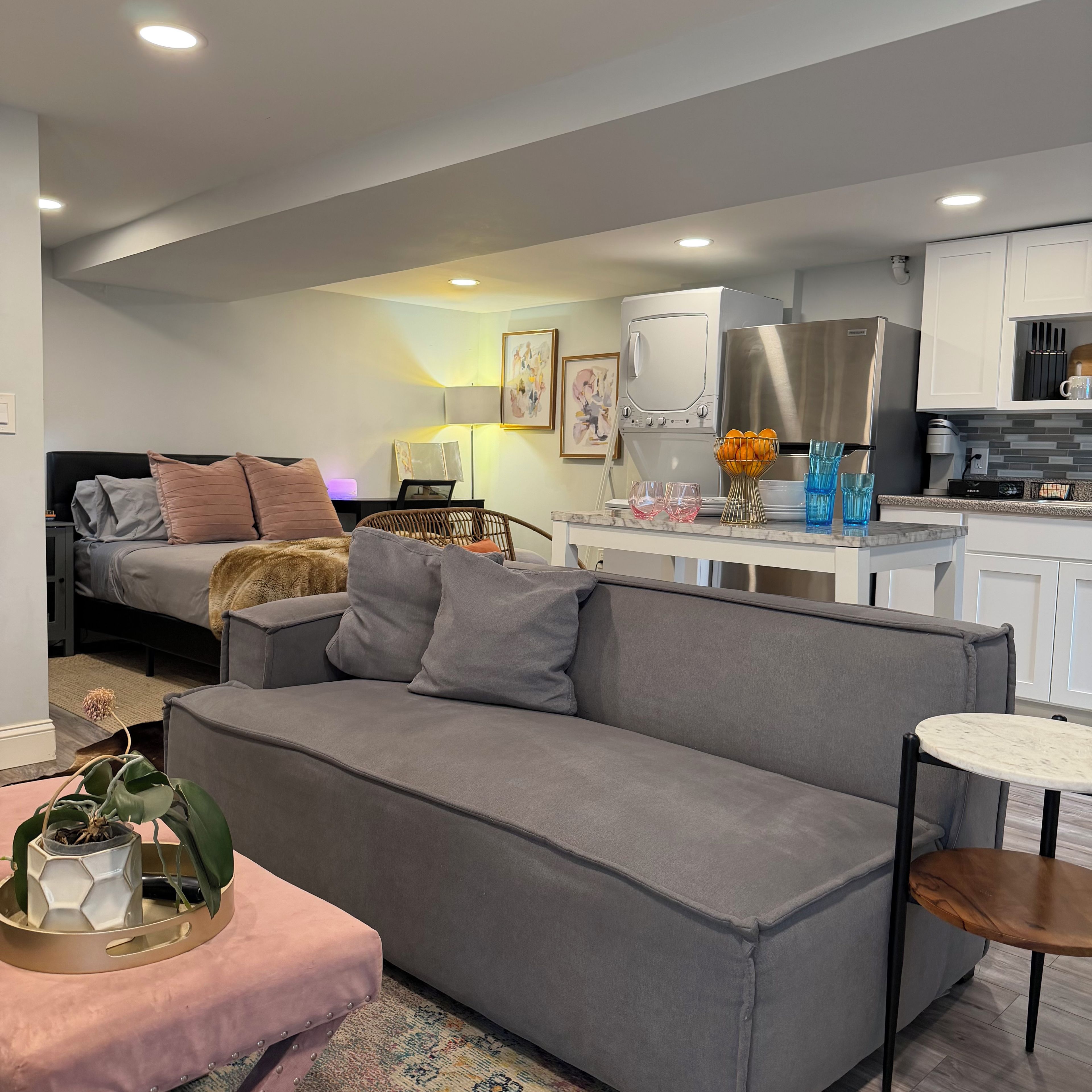 A modern living room with a grey sofa, a small round table, and a kitchen area with white cabinets and appliances.