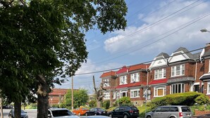 Une rue résidentielle bordée de voitures garées, avec un trottoir et des maisons aux toits rouges.